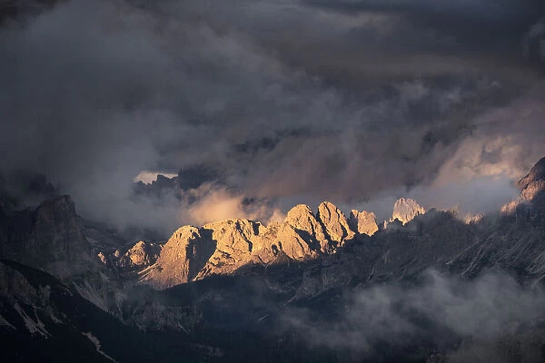 Light rays hitting Dolomites mountain peaks at sunset, surrounded by low clouds and mist, Cortina d Ampezzo, Dolomites, Veneto, Italy, Europe