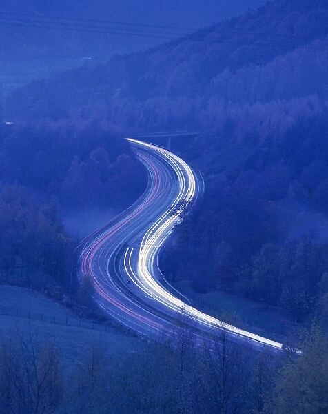 Light trails on rural road at twilight through woods in the Lake District