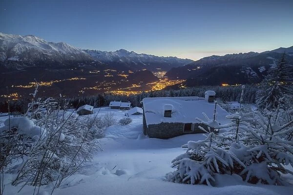 Lights of dusk illuminate the valley and the snow covered huts, Tagliate Di Sopra