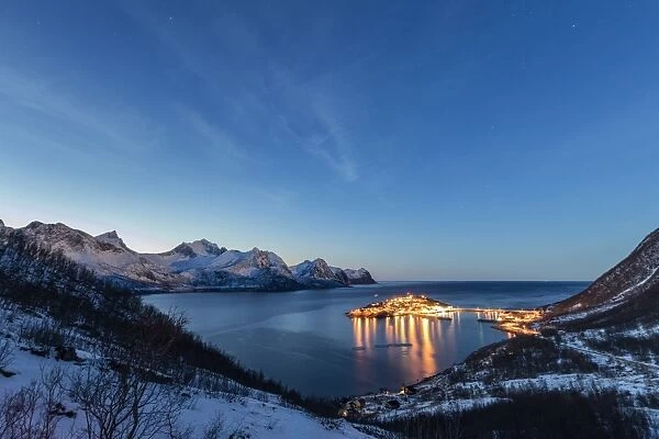 Lights on the typical fishing village framed by the frozen sea at dusk, Husoy, Fjordbotn