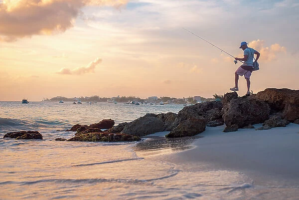 A local fisherman at sunset with calm water and orange sky on the south coast of Barbados, West Indies, Caribbean, Central America