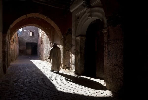 Local man wearing a djellaba casting a long shadow in a sunlit street in the Kasbah, Marrakech, Morocco, North Africa, Africa