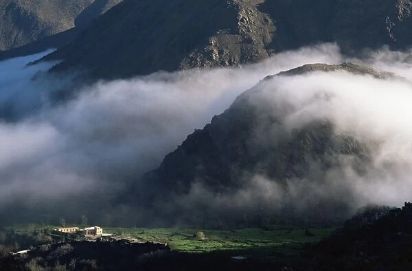 Local school below mist rising in valley of the High Atlas mountains