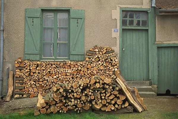 Logs piled outside a traditional cottage with shutters at the window, at Meuse