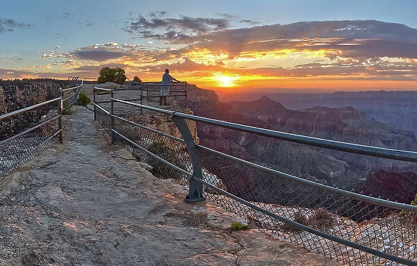 A lone hiker on Angels Window Overlook at Grand Canyon North Rim Arizona looking out at the sunrise