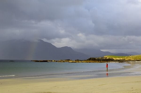 Lone person on a sandy beach under a stormy sky