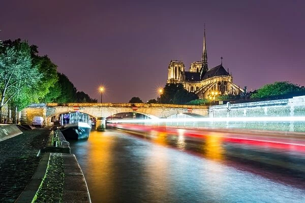 Long exposure of a boat on the River Seine passing Notre Dame Cathedral on a wet evening in Paris