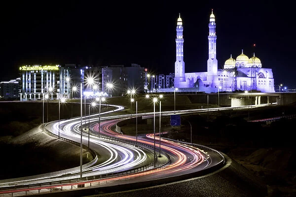 Long exposure cityscape night shot with a blue mosque and a street with car trails