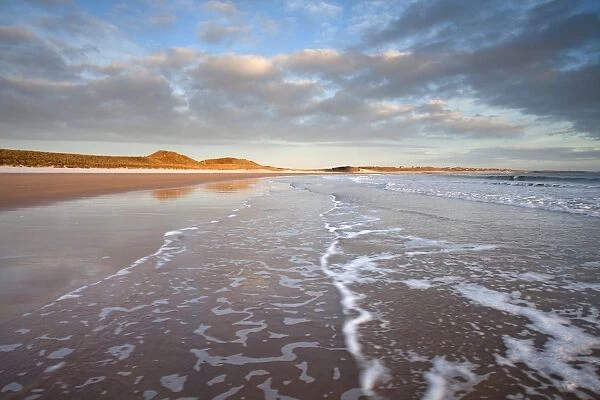 Looking across Embleton Bay just after sunrise towards the sunlit sand dunes at Embleton and Low Newton, with gentle waves washing up the beach in the foreground, Embleton, near Alnwick, Northumberland, England, United Kingdom, Europe