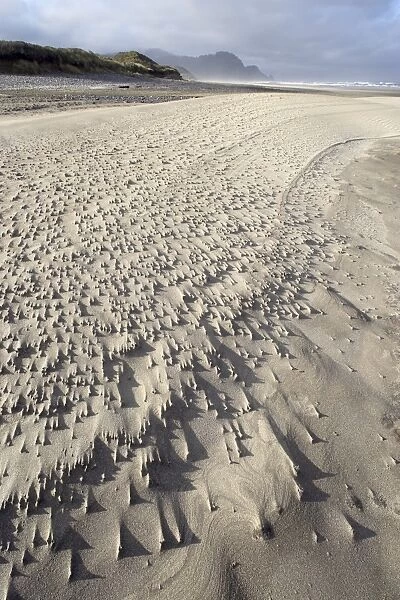 Looking along a windswept pebbly beach with sand trails