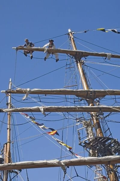 Detail of main mast of tall ship with two seamen on top yard securing sail