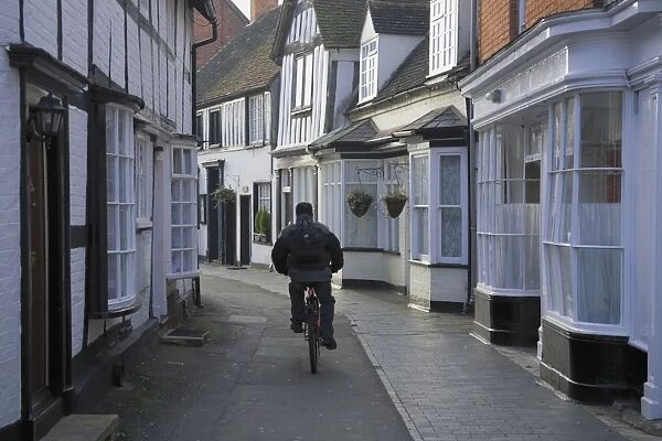 Man cycling along narrow street, Alcester, Warwickshire, Midlands, England