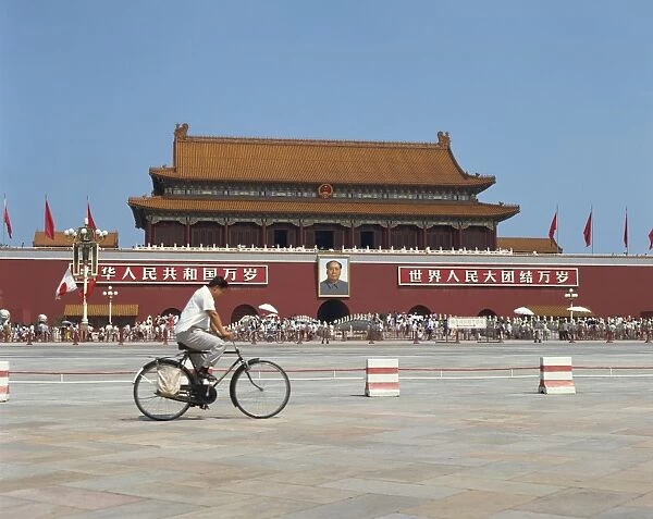 Man cycling through Tiananmen Square with portrait of Mao Tse Tung behind