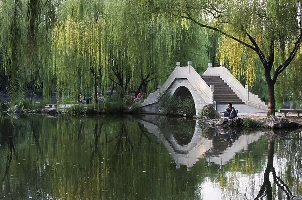 Man fishing next to a stone arched bridge in Zizhuyuan Black Bamboo Park