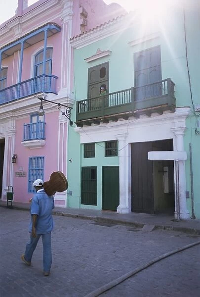 Man with guitar walking past coloured buildings in central Havana, Cuba