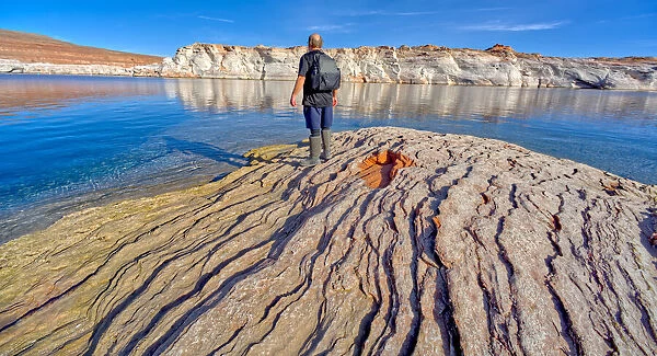 Man hiking along rocky shoreline of Lake Powell in an area called the Chains in the Glen