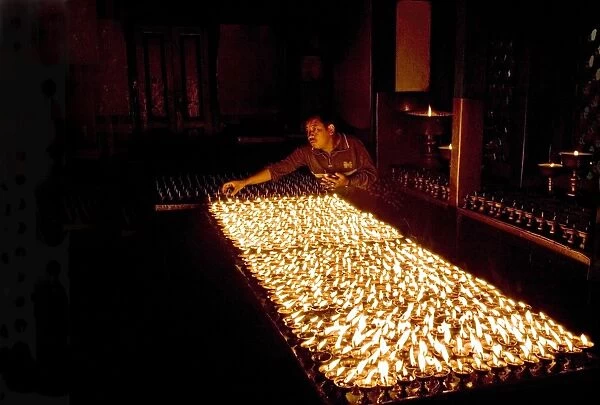 Man lights butter lamps in the early morning inside