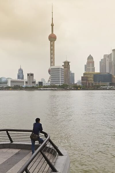 A man looking at the Oriental Pearl Tower and Pudong skyline across the Huangpu River from the Bund, Shanghai, China, Asia