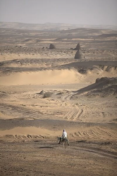 A man on mule-back traverses the desert around the