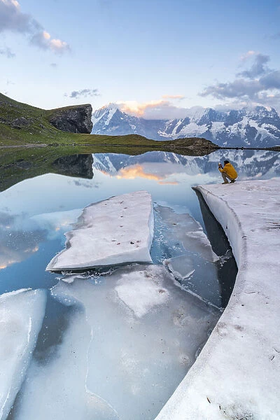 Man photographing Jungfrau mountain from frozen shores of Grauseeli lake at sunset