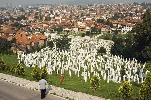 Man reflecting at cemetery overlooking city houses, Sarajevo, Bosnia, Bosnia-Herzegovina