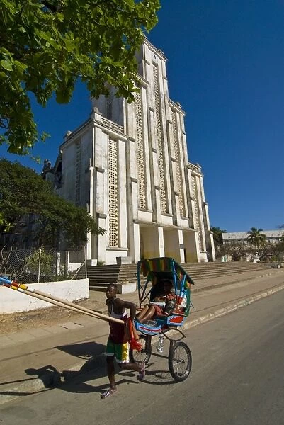 Man with a rickshaw in front of a modern church in Mahajanga, Madagascar, Africa