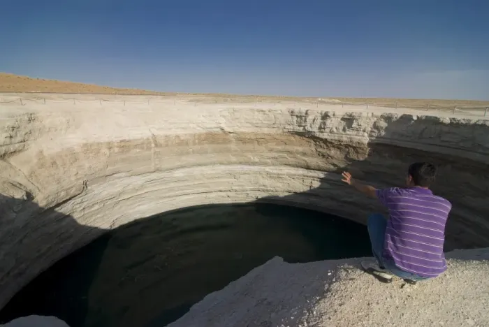 Framed Print : Man sitting on top of a crater filled with water, Karakol desert, Turkmenistan Framed Print : Man sitting on top of a crater filled with water, Karakol desert, Turkmenistan