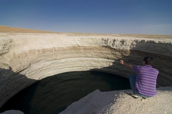 Man sitting on top of a crater filled with water, Karakol desert, Turkmenistan