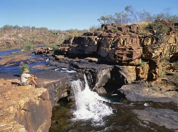 A man sitting on a rock up river, at the first stage of the Mitchell Falls in Kimberley