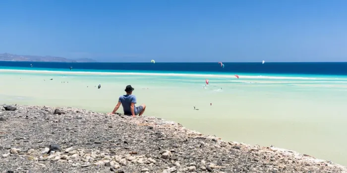 Framed Print : Man sitting on rocks looking at the kitesurfers in the clear sea, Sotavento beach, Jandia Framed Print : Man sitting on rocks looking at the kitesurfers in the clear sea, Sotavento beach, Jandia