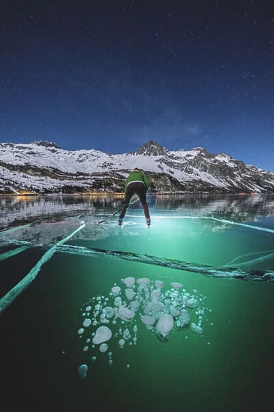 Man skating on frozen Lake Sils lit by head torch at night, Engadine