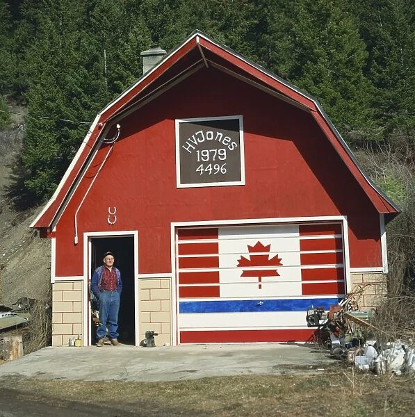 A man stands in the doorway beneath two lucky horseshoes, beside a door painted with the Canadian flag, at a patriotic workshop near Vernon, British Columbia, Canada