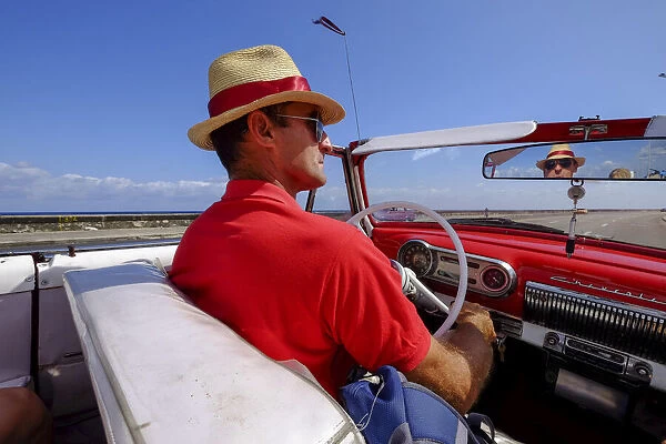 Man in straw hat drives vintage car along the Malecon, Havana, Cuba, West Indies