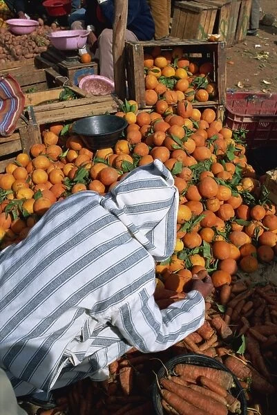 Man in traditional clothing sorting oranges and carrots