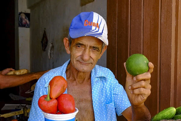 A man at a vegetable stand holds up a lime, Trinidad, Cuba, West Indies, Central America