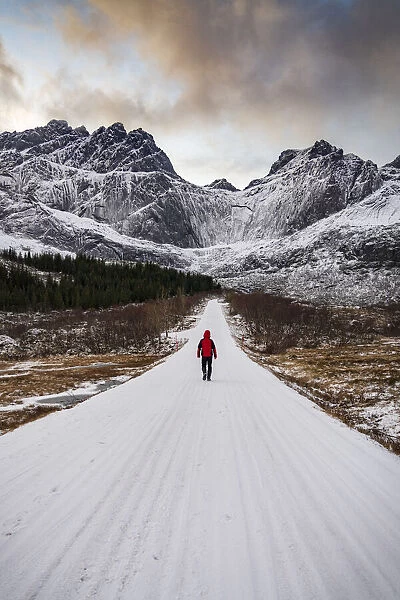 Man walking on empty mountain road covered with snow in winter, Nusfjord, Nordland county, Lofoten Islands, Norway, Scandinavia, Europe
