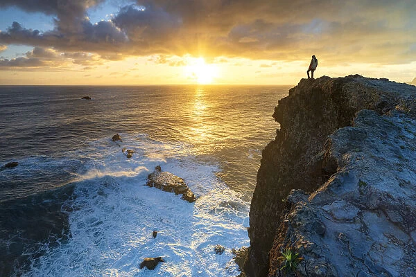 One man watching sunrise over the ocean waves from cliffs, Madeira island, Portugal