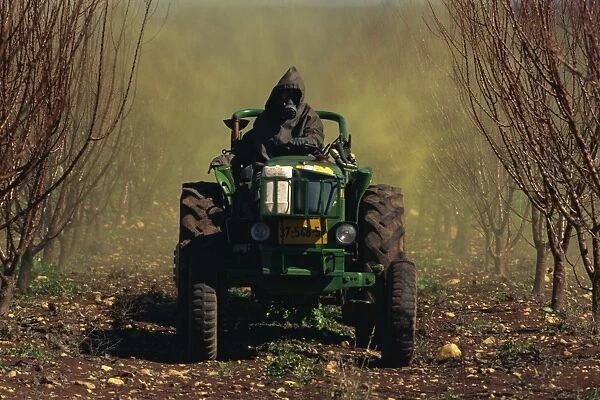 Man wearing protective clothing on a tractor spraying orchards in winter in Upper Galilee