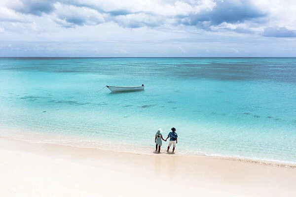 Man and woman holding hands on a tropical beach admiring the crystal clear sea, aerial view, Antigua and Barbuda, West Indies, Caribbean, Central America