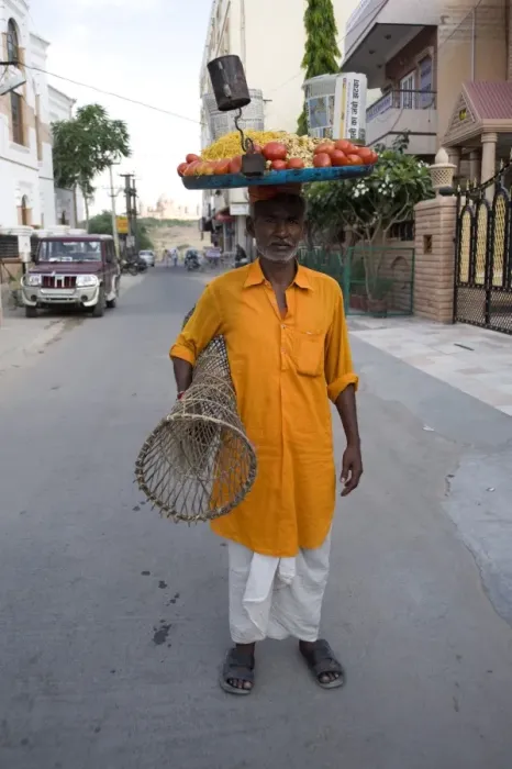 Framed Print : Man in yellow kurta with tray of snacks on his head and table under his arm