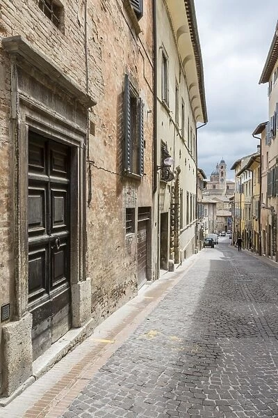 A medieval alley of the hill town with Piazza Duca Federico in the background, Urbino