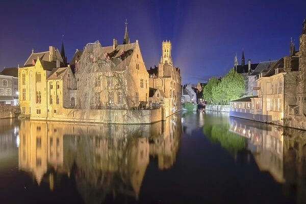 The medieval Belfry and historic buildings reflected in Rozenhoedkaai canal at night