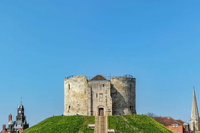 Framed Print : Medieval stone tower on a grassy hill with clear blue sky, flanked by church spires in the background, Clifford's Tower, York, North Yorkshire, England, United Kingdom, Europe