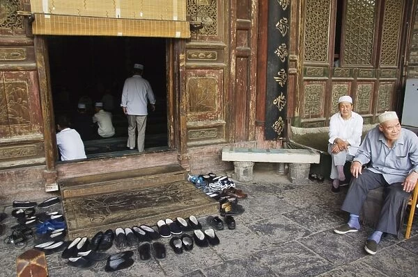 Men praying and shoes left outside at The Great Mosque located in the Muslim Quarter home to the citys Hui community, Xian City, Shaanxi Province