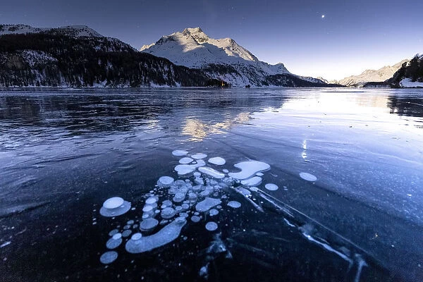 Methane bubbles in the icy surface of the lake with snowy peak illuminated by moonlight