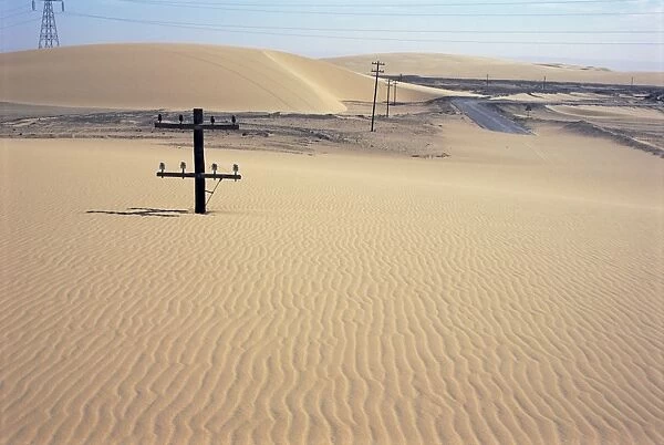 Migrating barchan sand dunes across road marked by buried telegraph poles