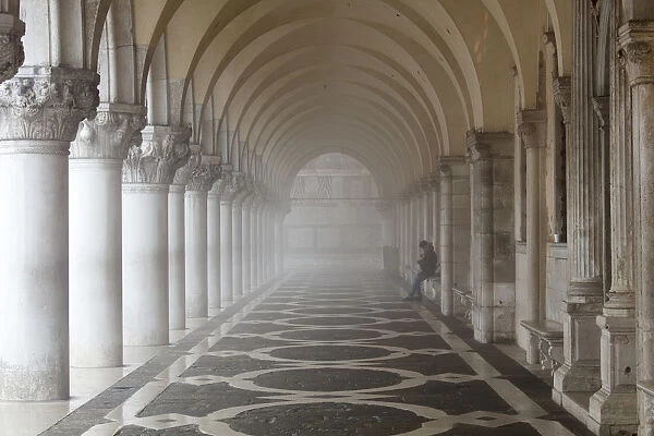 Misty view of pillars with lone woman sitting, Doges Palace, St. Marks Square, Venice