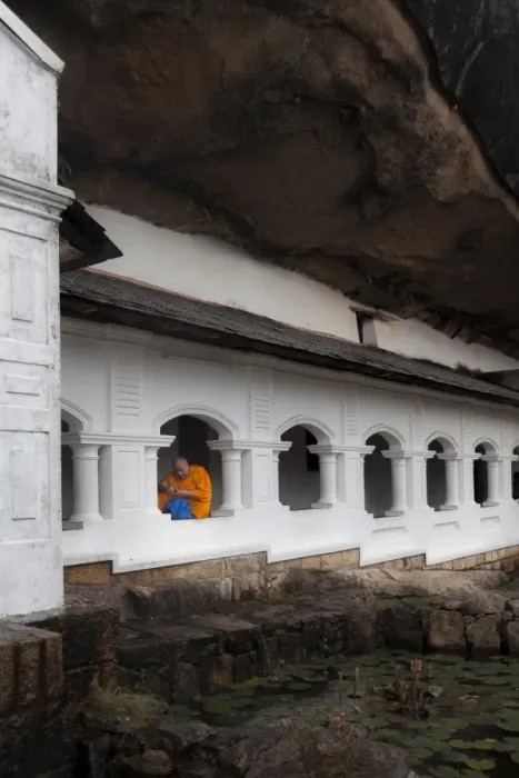 Framed Print : A monk sits and looks at his phone beneath shelter, Royal Rock Temple, Golden Temple of Dambulla, UNESCO World Heritage Site, Dambulla, Sri Lanka, Asia