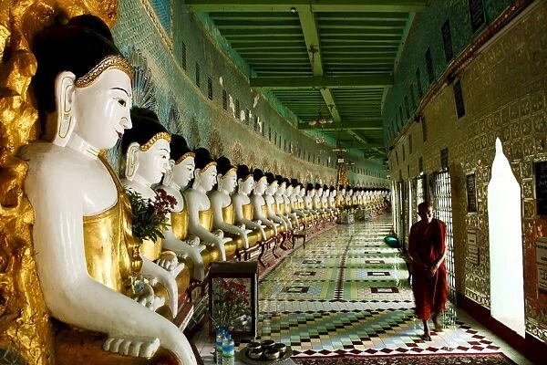 Monk walking past Buddha statues in a crescent shaped colonnade in Umin Thounzeh