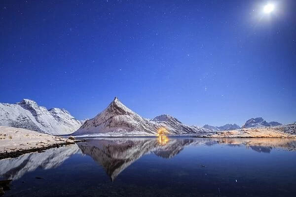 Full moon and stars light up the snow capped peaks reflected in sea, Volanstinden